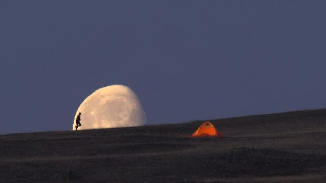 Silhouette of a running man on a mountain slope against big moon and night sky 