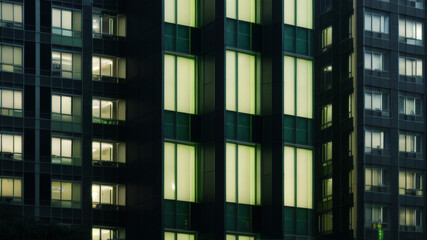 Obraz premium Modern Building Facade with Green Illuminated Windows at Night
