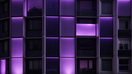 Contemporary high-rise building illuminated with vibrant purple window lights against a dark night sky. The symmetrical glass facade and bold lighting create a futuristic and stylish urban atmosphere