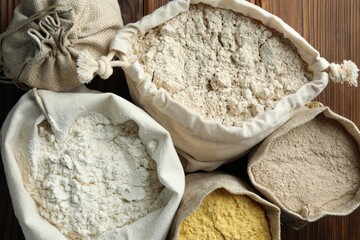 Different types of flour in bags on wooden table, flat lay