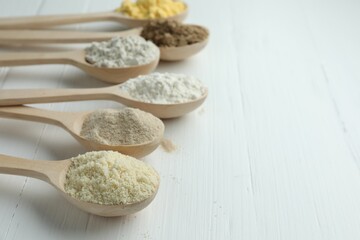 Different types of flour in spoons on white wooden table, closeup. Space for text