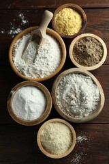 Different types of flour in bowls on wooden table, flat lay