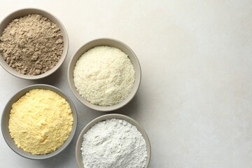 Different types of flour in bowls on light grey table, flat lay. Space for text