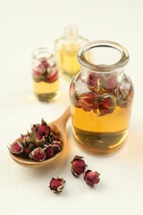 Open perfume bottles with aromatic essential oils and dried roses on white table, closeup