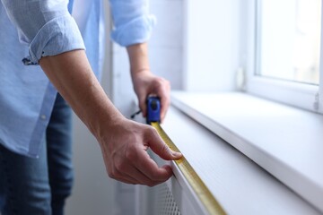 Man measuring windowsill with tape indoors, closeup