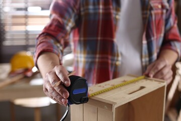 Man measuring wooden shelf with tape indoors, closeup