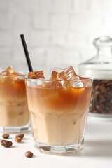 Tasty iced coffee and beans on white table, closeup