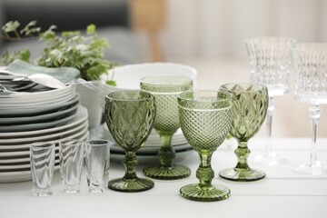 Clean glasses, plates, cutlery and green houseplant on white wooden table indoors