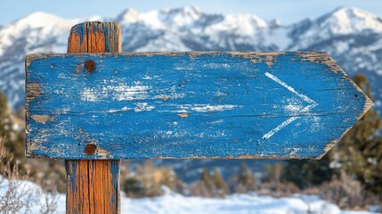 Aged wooden directional sign against snowy mountain backdrop.