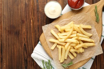 Tasty french fries served with sauces and rosemary on wooden table, flat lay. Space for text