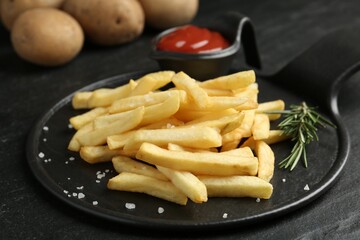 Tasty french fries served with ketchup and rosemary on black table, closeup