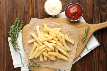 Tasty french fries served with sauces and rosemary on wooden table, flat lay