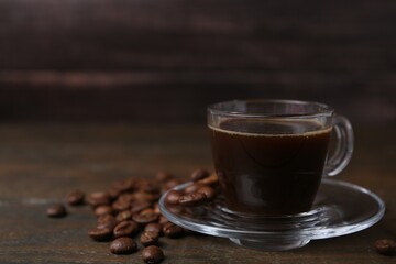 Aromatic coffee in glass cup and beans on wooden table, closeup. Space for text