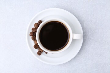 Aromatic coffee in cup, beans and saucer on light table, top view