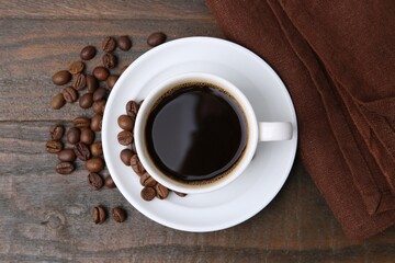 Aromatic coffee in cup, beans and saucer on wooden table, flat lay