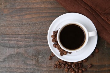 Aromatic coffee in cup, beans and saucer on wooden table, flat lay. Space for text