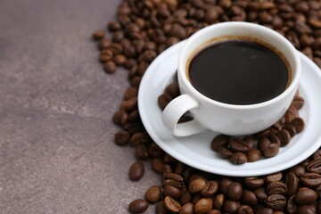 Aromatic coffee in cup, saucer and beans on brown textured table, closeup. Space for text