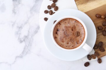 Aromatic coffee in cup, beans and saucer on white marble table, top view. Space for text