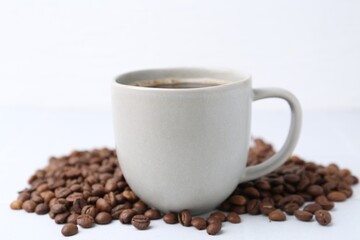 Aromatic coffee in cup and beans on white background, closeup