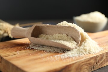 Pile of flour and scoop on dark wooden table against black background, closeup