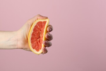 Woman squeezing grapefruit on pink background, closeup. Space for text