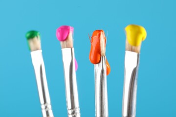 Many brushes with color paints on light blue background, closeup