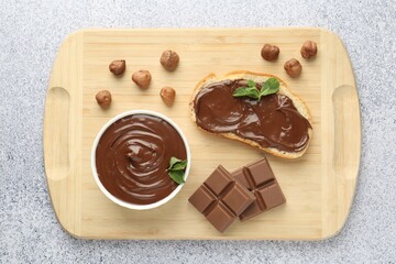 Tasty chocolate spread, toast, hazelnuts and mint on grey textured table, top view