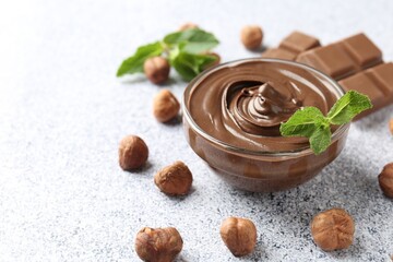 Tasty chocolate spread with mint in bowl and hazelnuts on grey textured table, closeup. Space for text