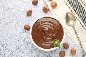 Tasty chocolate spread with mint in bowl and hazelnuts on grey textured table, flat lay