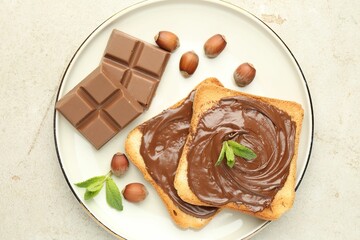 Toasts with tasty chocolate spread, pieces, mint and hazelnuts on light table, top view