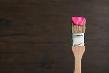 Brush with pink paint on wooden background, closeup. Space for text