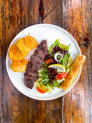 Overhead view of plated steak with potatoes and salad on a wooden surface.