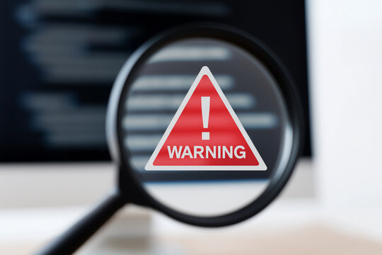 Cybersecurity Alert – Magnifying Glass Focusing on Warning Sign and Code on Screen