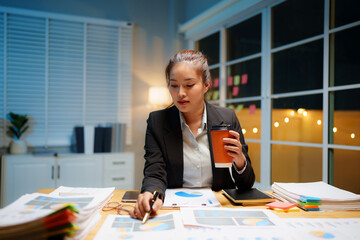 Dedicated businesswoman working late at night in a dimly lit office, focused on her laptop amidst...