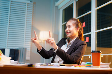 Dedicated businesswoman working late at night in a dimly lit office, focused on her laptop amidst...