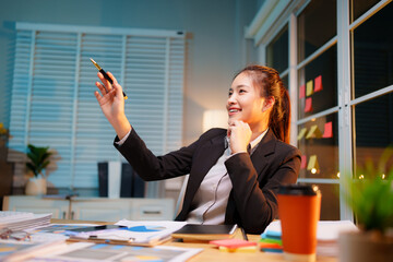 Dedicated businesswoman working late at night in a dimly lit office, focused on her laptop amidst...