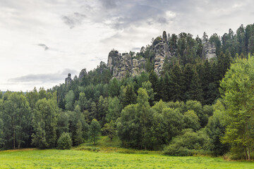 Landscape of Adrspach-Teplice Rocks area, in Hradec Kralove Region in the Czech Republic, Europe. Rock formations towering above lush forest under cloudy sky. Serene natural landscape, peaceful vista.
