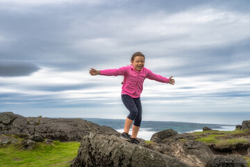 A Joyful Girl is Happily Balancing on a Rocky Outcrop with a Beautiful and Dramatic Sky right...