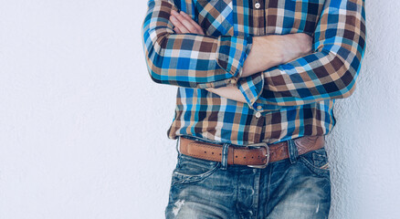 Man in a checkered shirt. Guy in jeans with a leather belt. Man with a beard stands with folded arms. Style and fashion