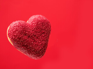 Obraz premium Red creative heart shaped donut floating in the air, red color saturated background. Love and romance concept. Valentine gift idea. Transforming food for marketing reasons to increase sales.