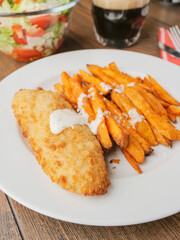 Popular fish and chips meal on a white plate and brown wooden table. Chips are made from sweet...