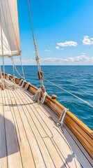 A wooden sailboat deck with a white sail and blue ocean in the distance