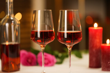 Glasses of red wine and burning candles against blurred background, closeup. Romantic dinner