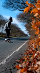 Fototapeta premium Person skateboarding on a sunny road lined with autumn leaves
