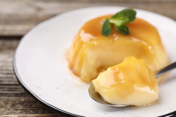 Delicious pudding with caramel sauce and mint served on wooden table, closeup