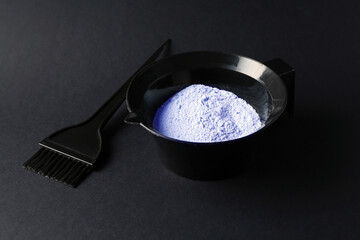 Bowl with hair bleaching powder and brush on black background, closeup