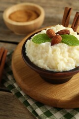 Delicious rice pudding with almonds, mint and cinnamon sticks on wooden table, closeup