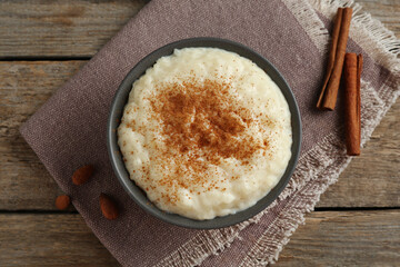 Delicious rice pudding with cinnamon and almonds on wooden table, flat lay