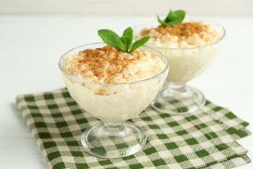Delicious rice pudding with cinnamon and mint in glass dessert bowls on white table, closeup
