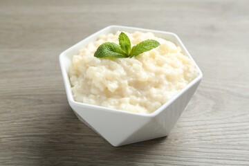 Delicious rice pudding and mint in bowl on wooden table, closeup